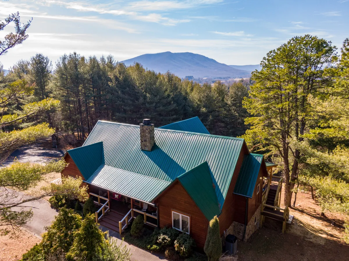 This exterior shot features the house with its distinctive green roof, nestled among lush trees and set against a stunning mountain backdrop. The peaceful, inviting vibe highlights the home’s connection to nature and its ideal location for launching local adventures.