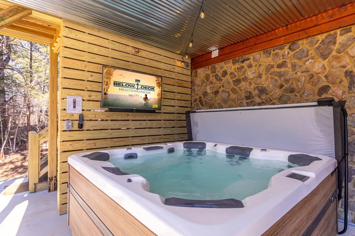 A cozy interior view of a hot tub area with wood and stone accents, a television, and space for friends to gather, capturing the promise of private relaxation and sociable evenings.