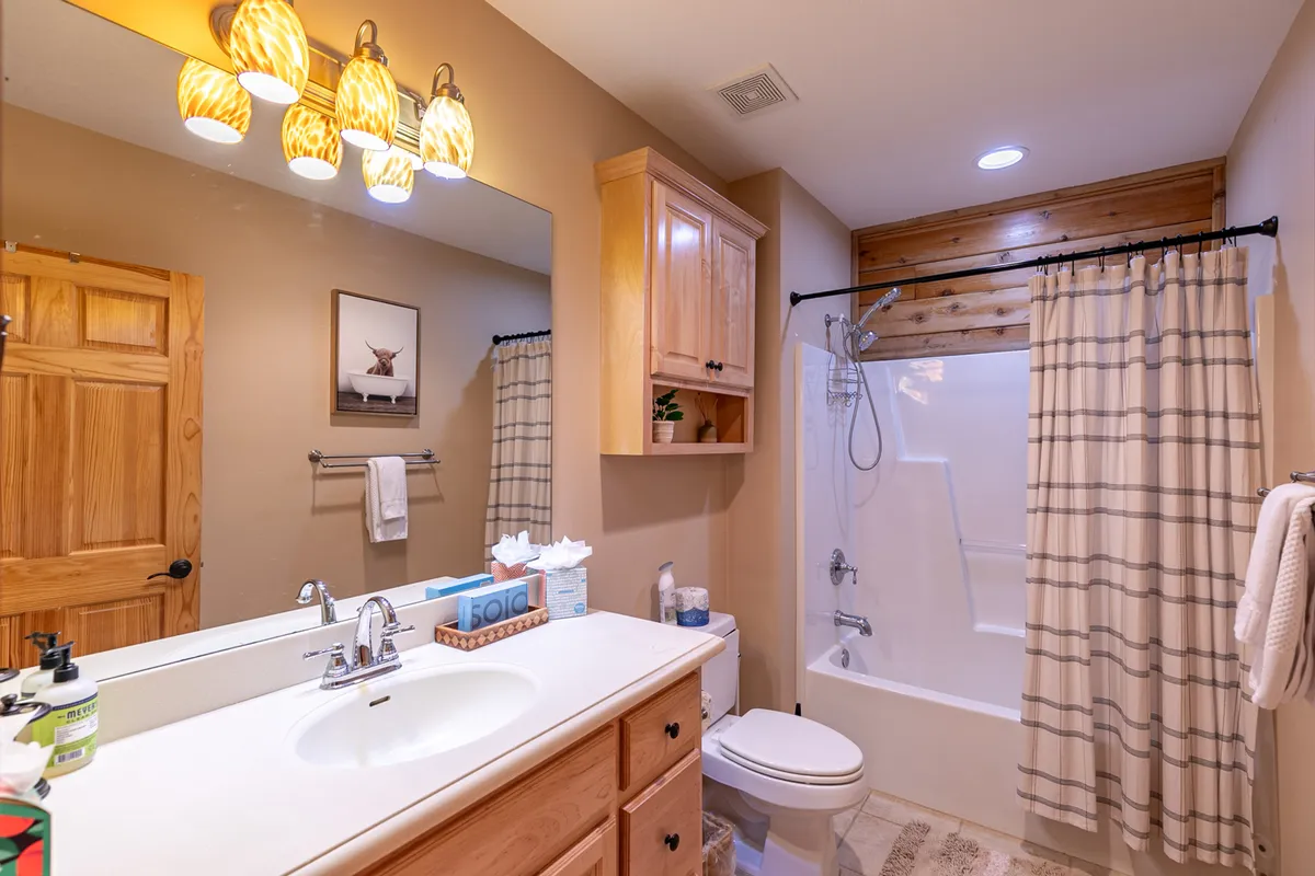 A well-appointed bathroom with a vanity sink, shower area, decorative light fixtures, and wooden cabinetry. The space exudes a sense of calm and modern convenience suitable for self-care routines and relaxing baths.