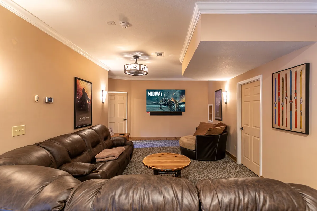 A cozy lounge area with a large leather sofa facing a television screen ready for a movie marathon. Movie posters on the wall and a wooden coffee table make this a perfect spot for relaxing after games, streaming shows, or hosting a movie night with friends and family.