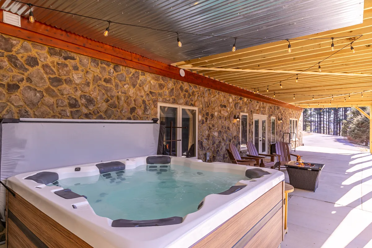A tranquil outdoor setting with a hot tub positioned against a stone wall, surrounded by string lights and cozy outdoor seating. The scene is inviting, with touches that encourage relaxation, stargazing, and gathering during evenings—an ideal place to wind down after a day of play.