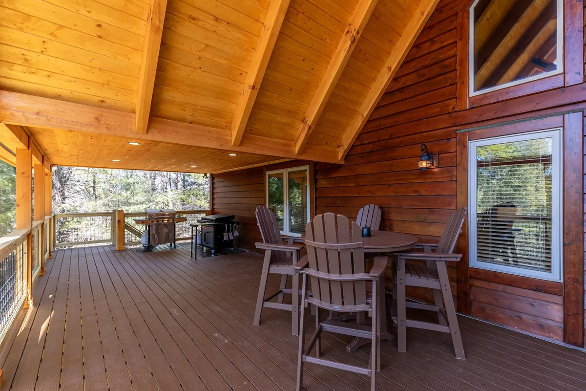 A wooden deck featuring an outdoor dining set and a barbecue grill, surrounded by natural scenery. The setup invites guests to dine outdoors or cook meals while enjoying the mountain breeze.
