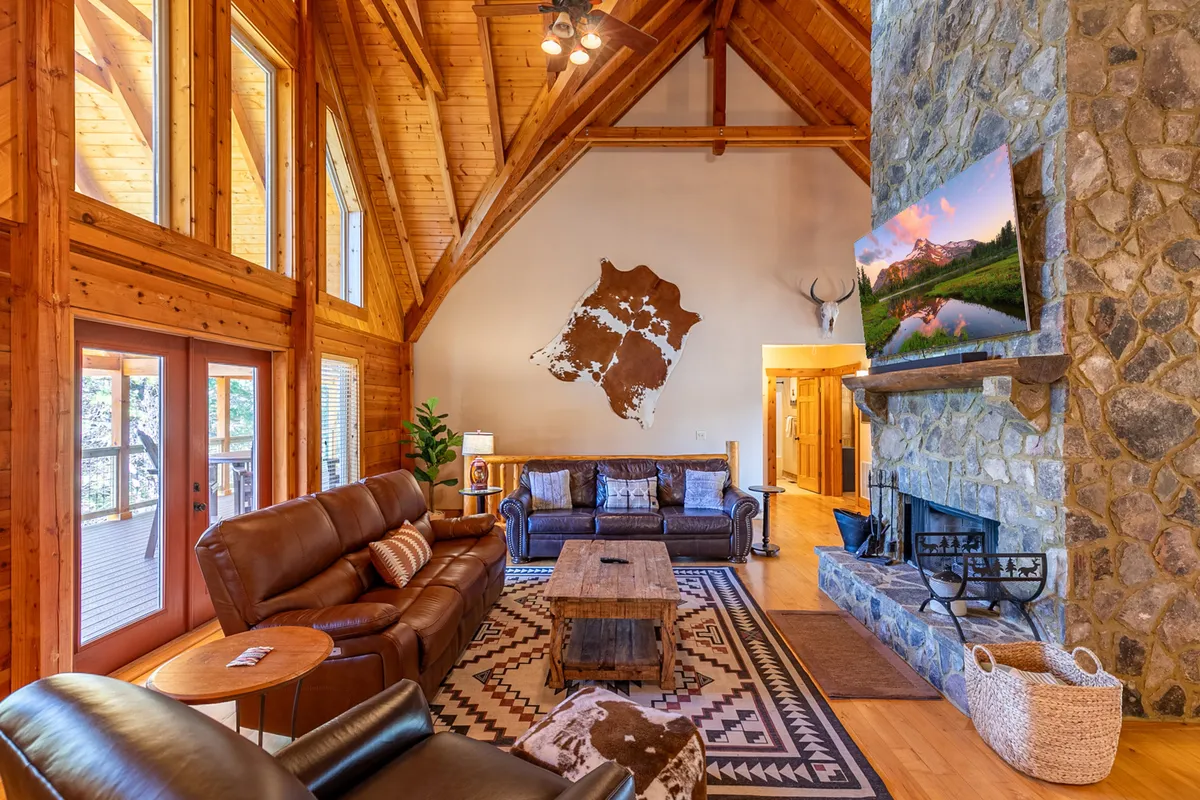 A comfortable living area featuring a prominent stone fireplace, large windows, wooden beams, and a plush sofa set. The arrangement creates a cozy nook for family movie nights, game sessions, or simply warming up after outdoor adventures, framed by decorative wall art for added homeliness.