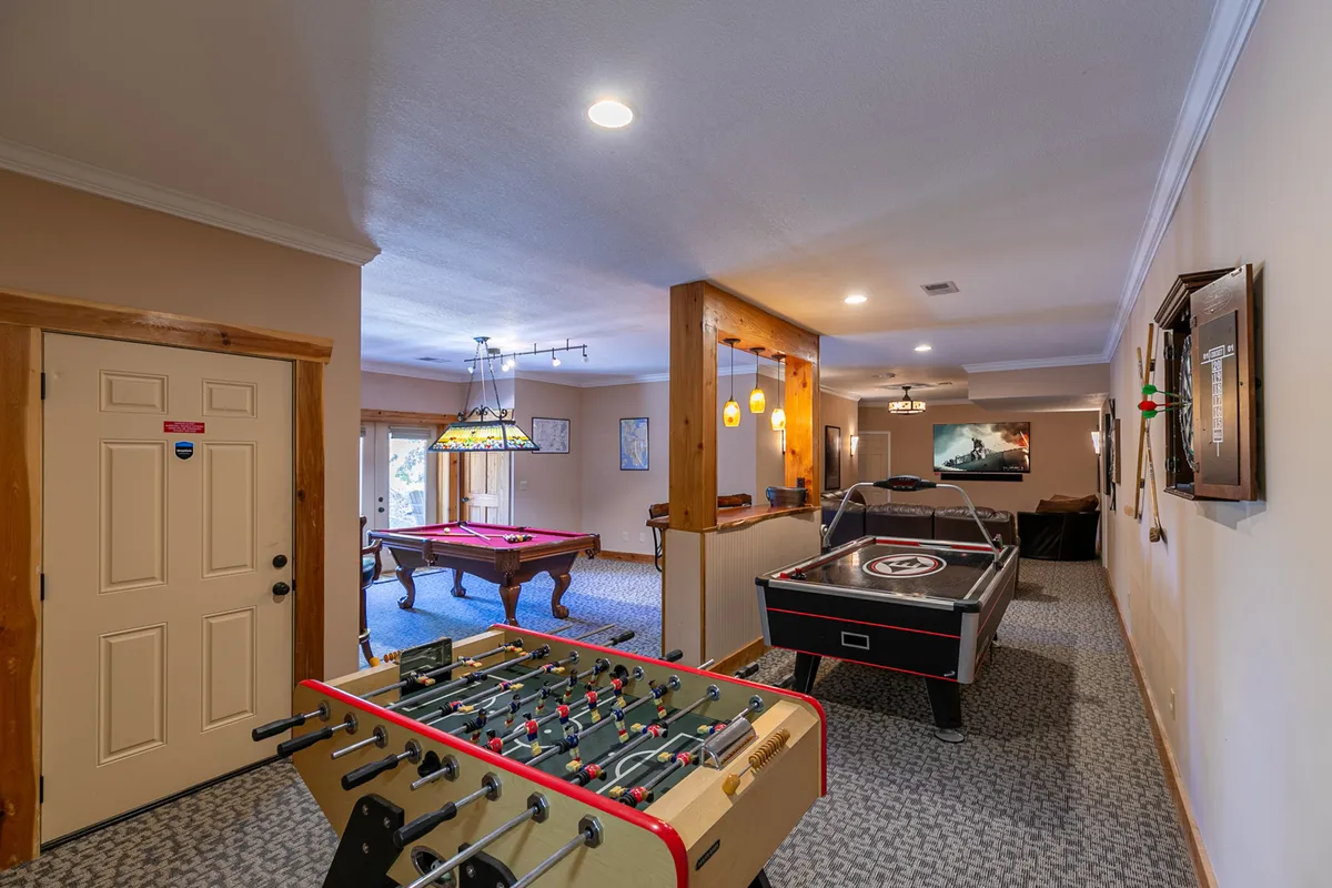 This image showcases a dedicated game room complete with a foosball table, pool table, and air hockey table. The space has a casual lounge area, inviting guests to relax and socialize between games. The furnishings and layout create a lively, communal atmosphere ideal for group entertainment.