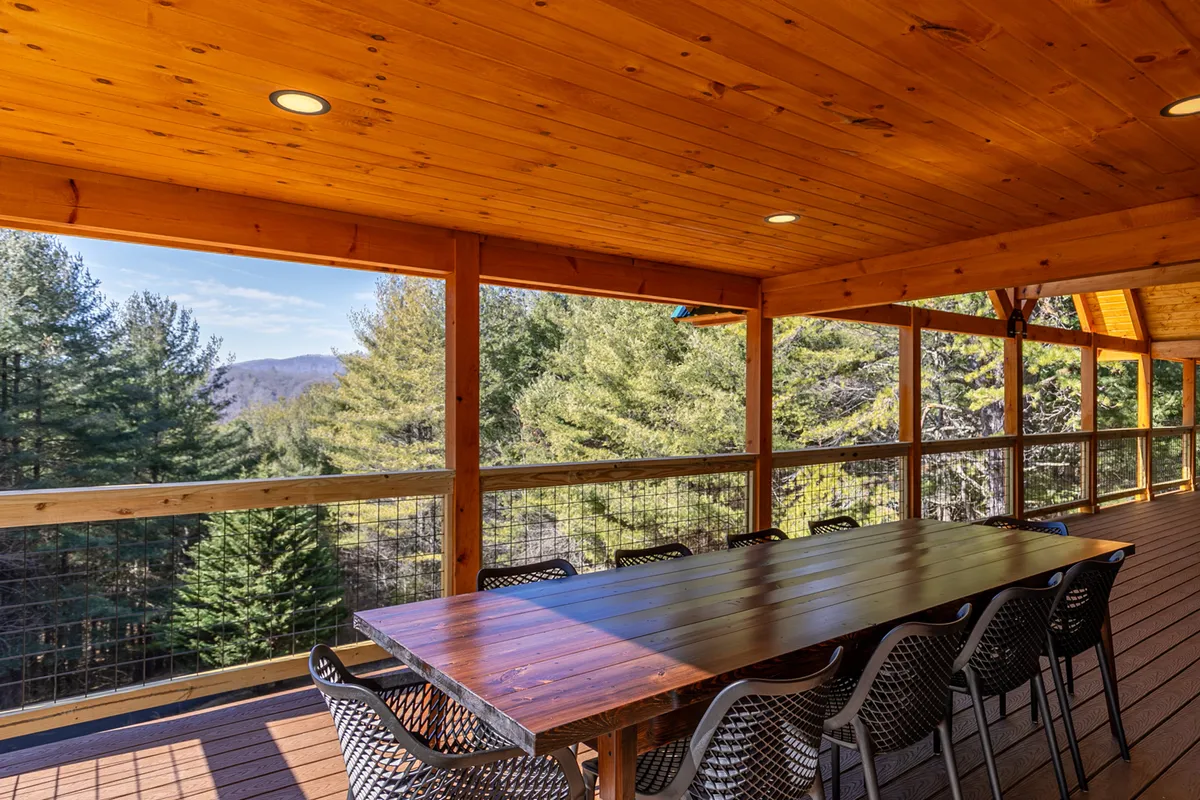A spacious wooden deck with a long dining table and outdoor seating, overlooking a panoramic mountain view. The setting is ideal for al fresco meals, social gatherings, and enjoying natural surroundings at sunset or under the stars.