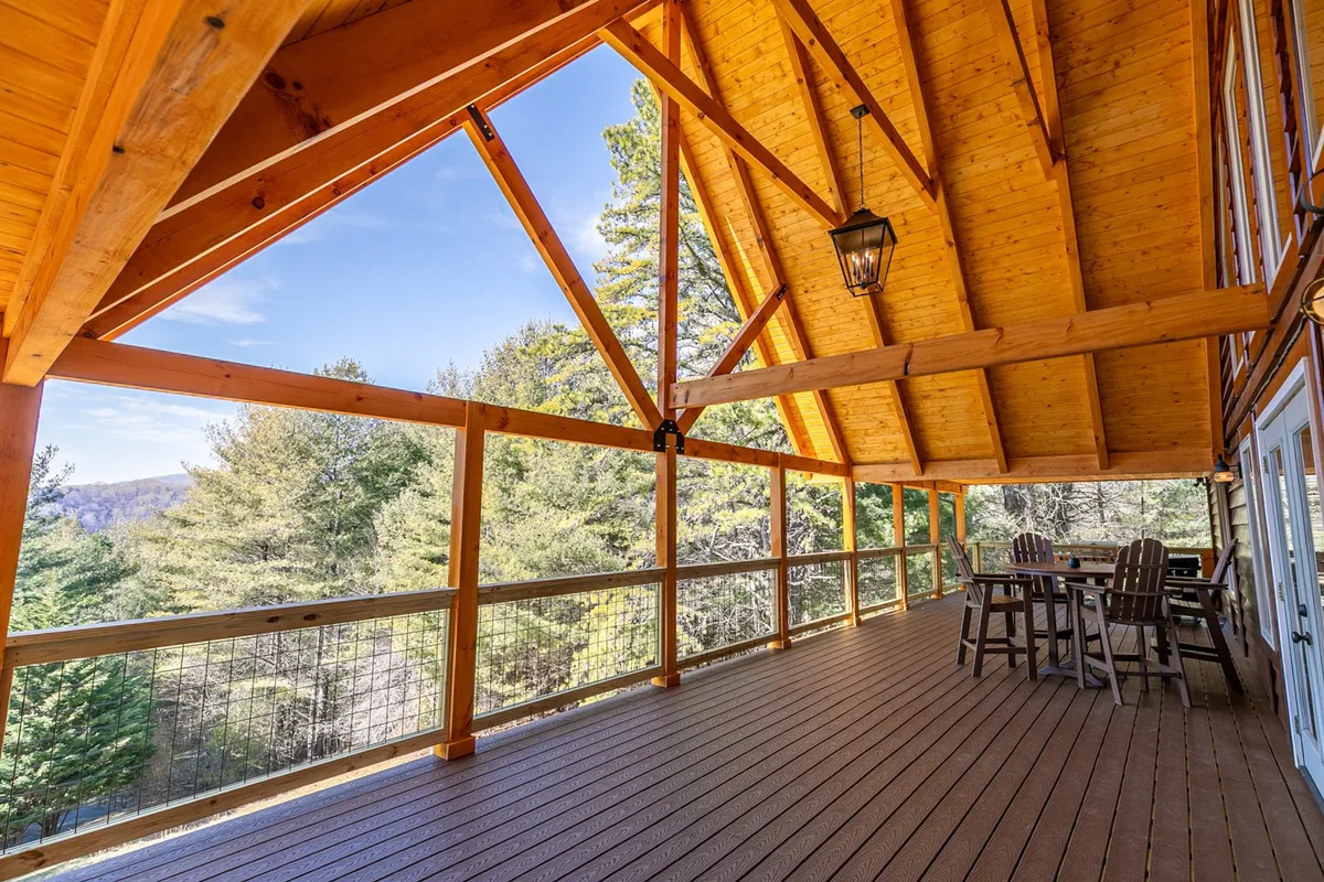 A tranquil exterior deck scene featuring wooden beams, comfortable deck furniture, and a scenic view of the natural surroundings. The space is open and inviting, perfect for relaxing outdoors with a pet or enjoying meals al fresco.